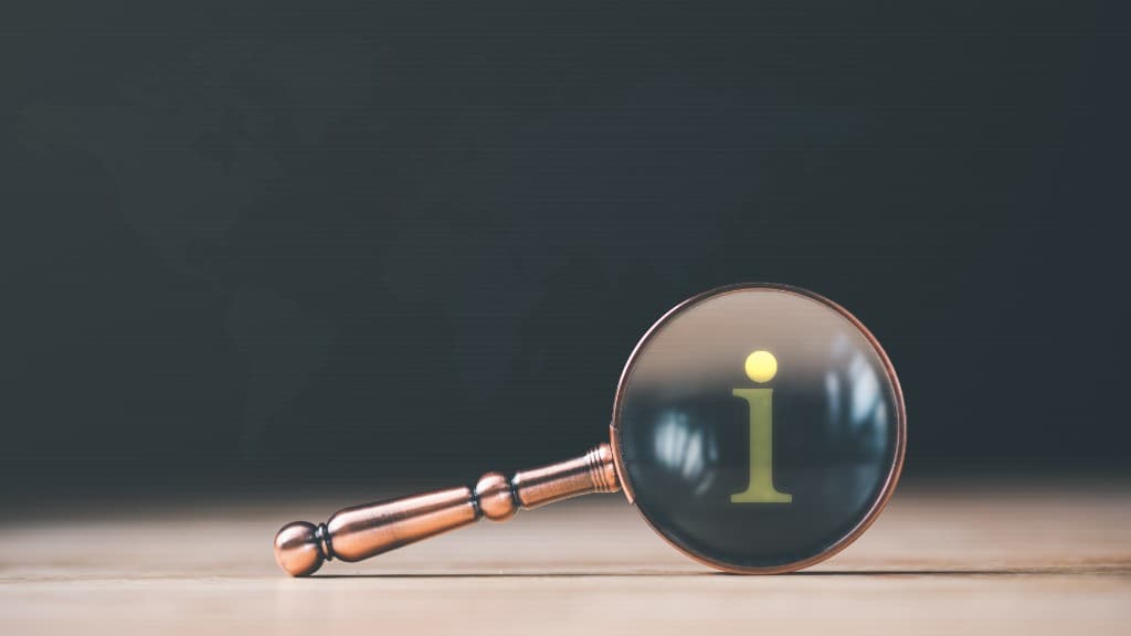 Magnifying glass on a desk with a glowing information icon in the lens